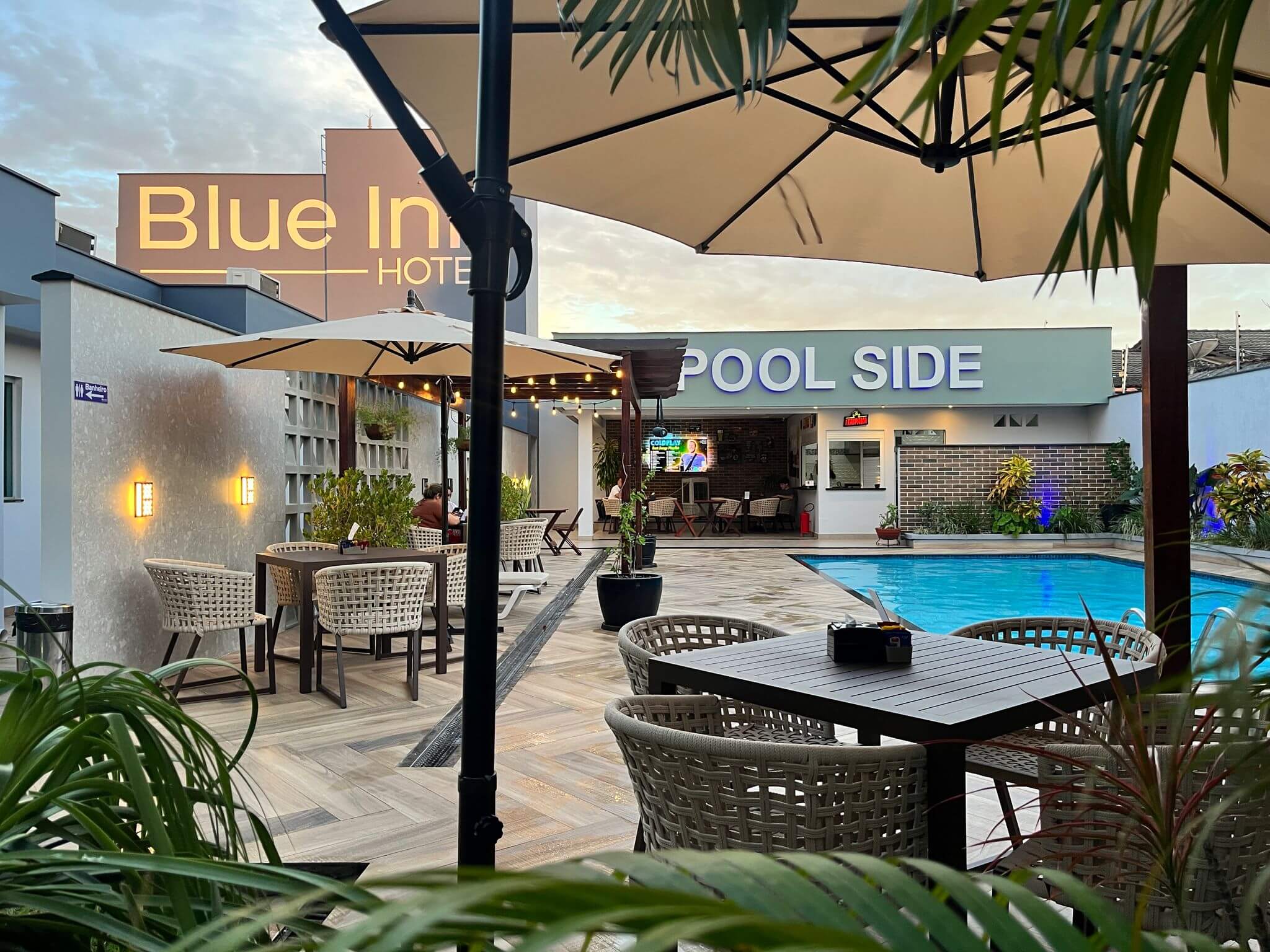 Área da piscina do Hotel Blue Inn ao entardecer, com o bar Pool Side ao fundo